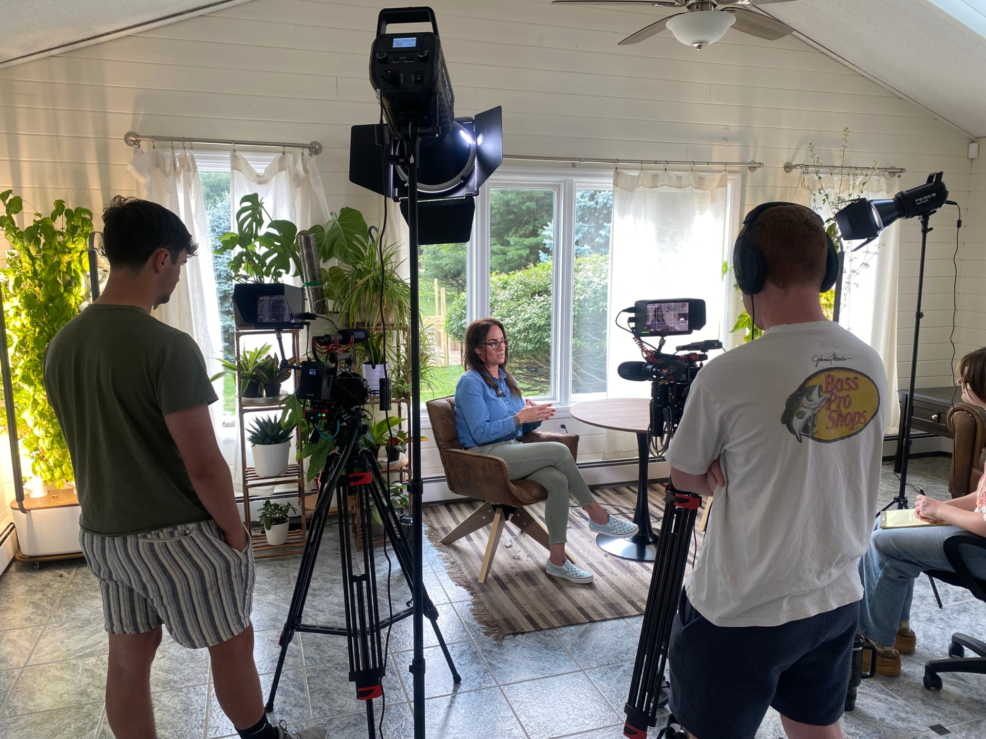 Crew filming a seated interview in a sunlit room surrounded by plants