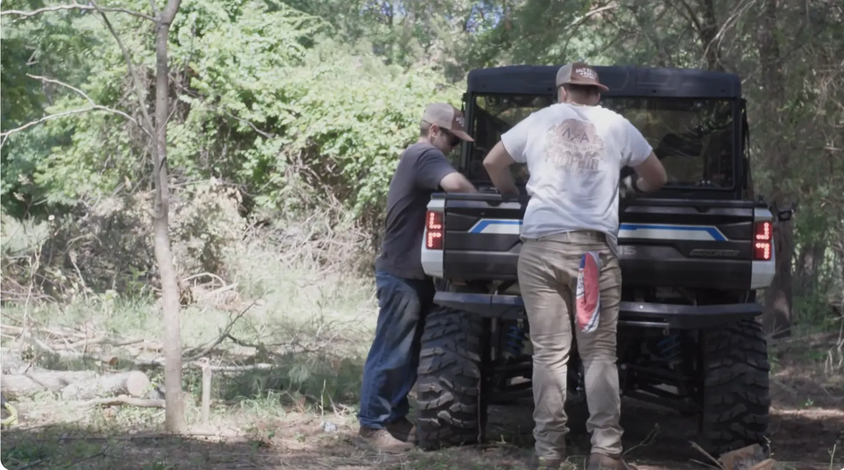 Two workers at the back of a utility vehicle in a wooded clearing