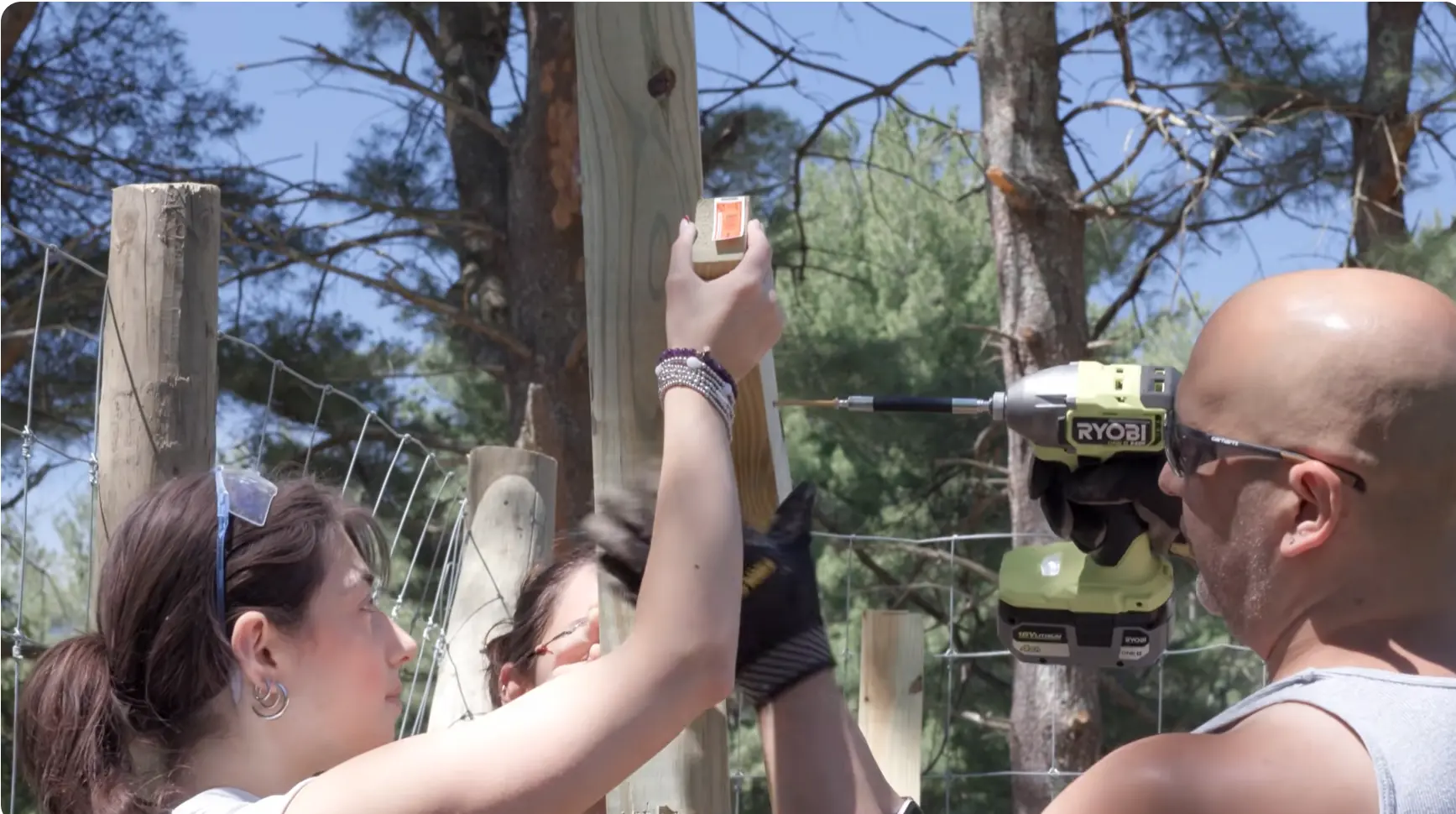 Volunteers fastening a sign to a fence post with a drill