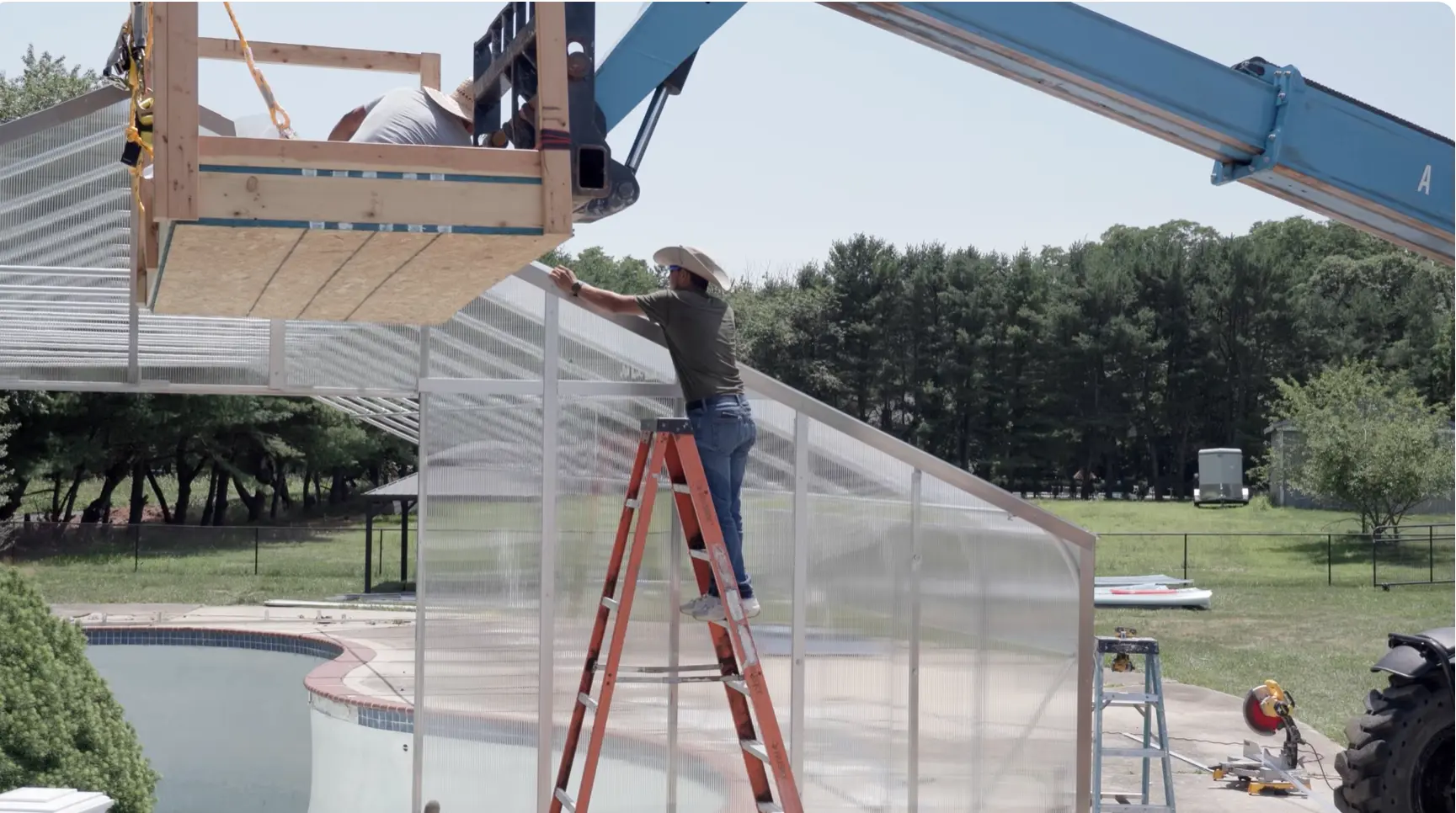 Crew assembling a greenhouse over an old swimming pool with a lift