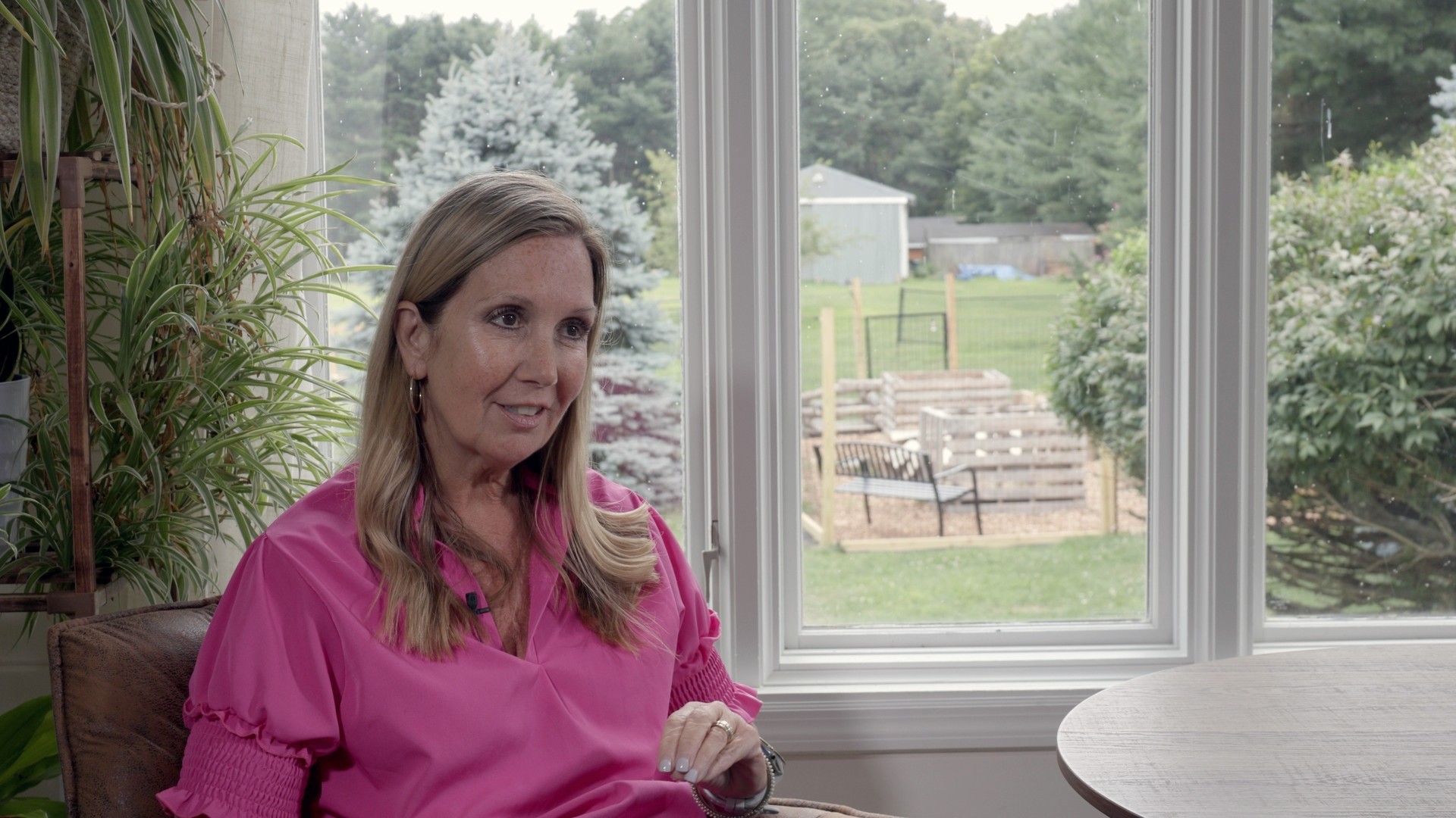 A woman in a pink blouse mid-sentence during a sit-down interview