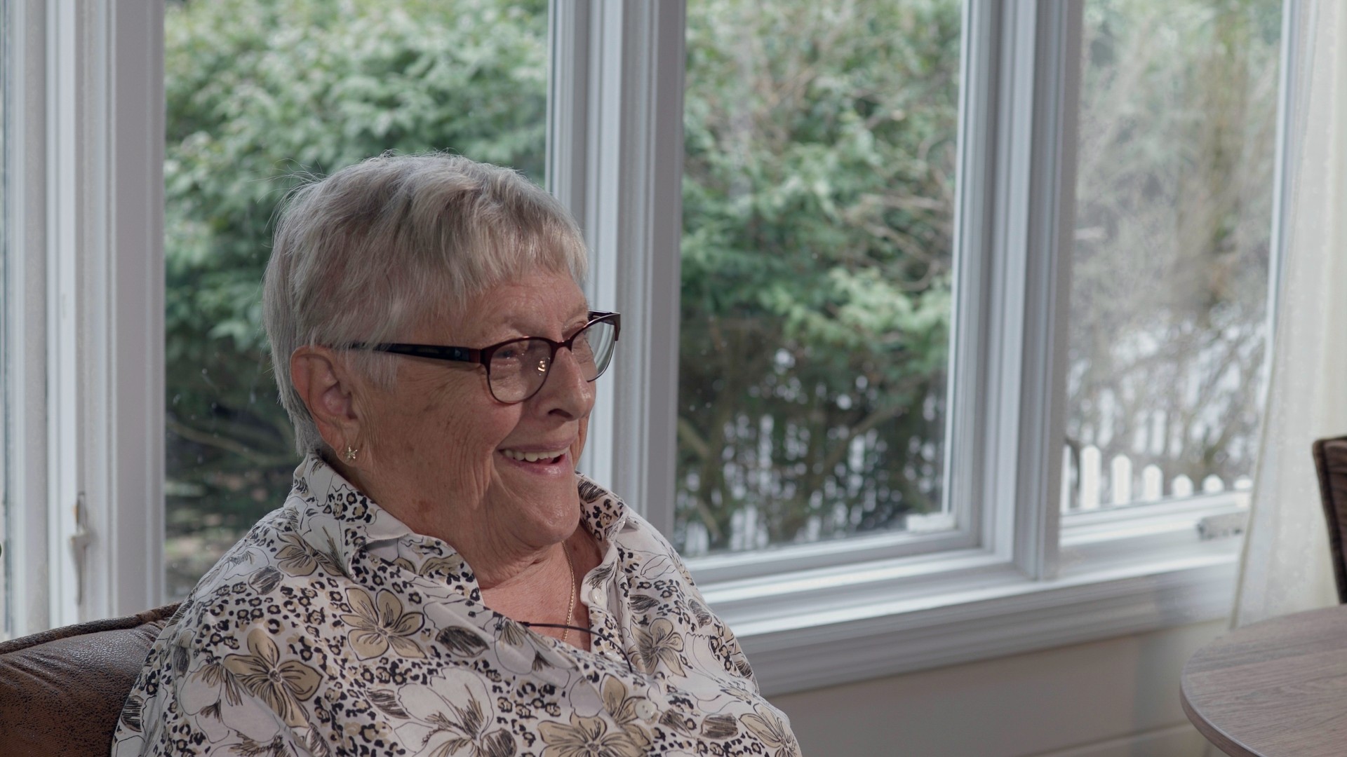 An older woman laughing during an interview in soft window light