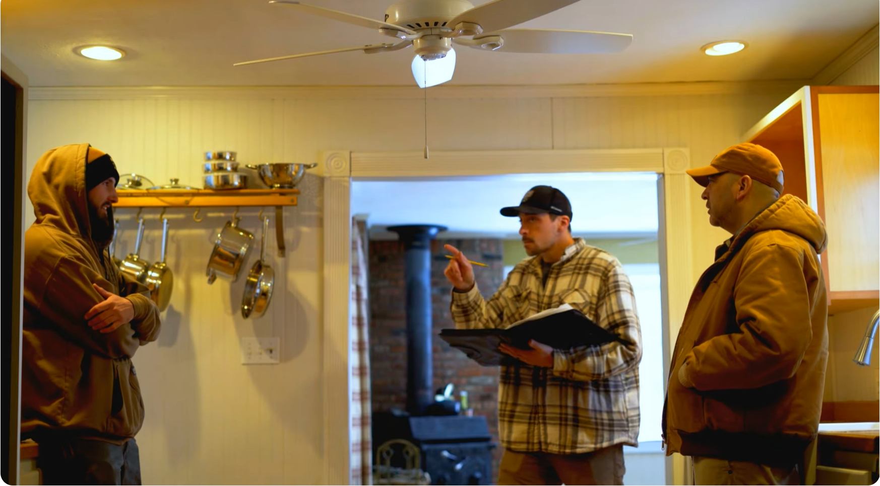Three men reviewing plans in a farmhouse kitchen